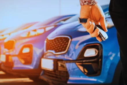 Woman holding car key looking at the parked rental cars.