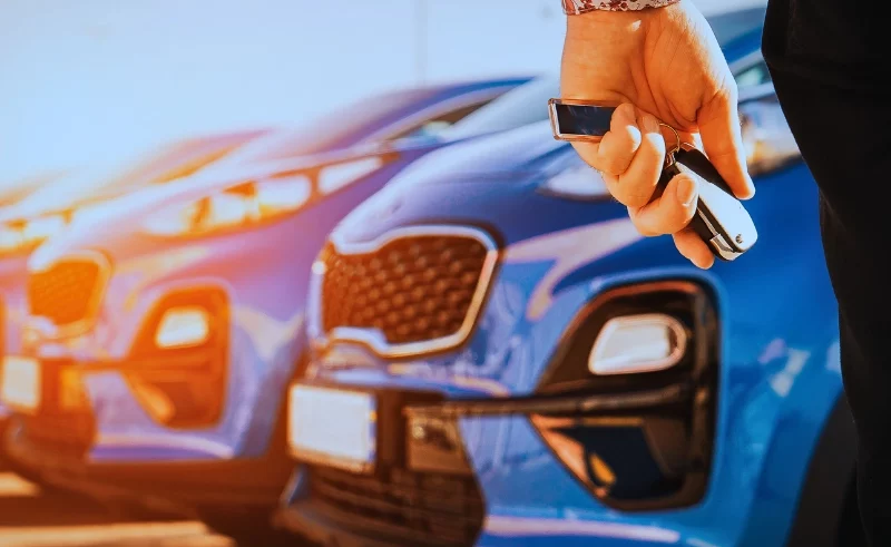 Woman holding car key looking at the parked rental cars.