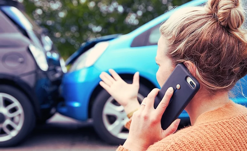 Distressed woman using her phone after a car accident.