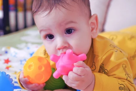 Baby on the crib putting his toys on his mouth.