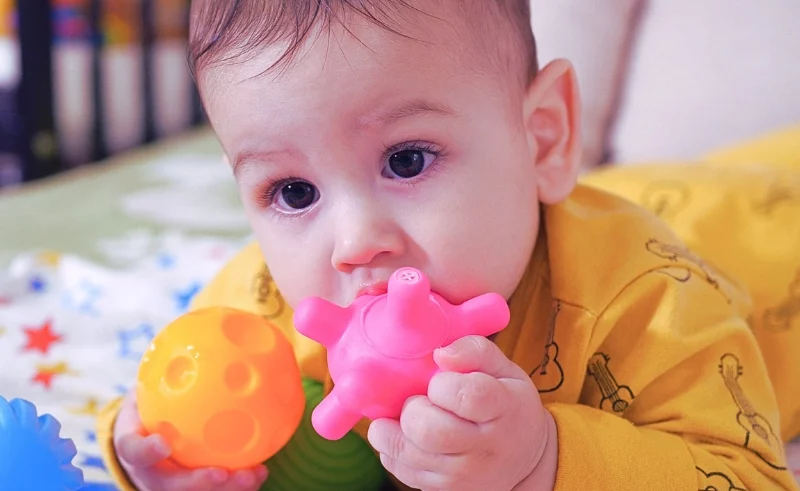 Baby on the crib putting his toys on his mouth.