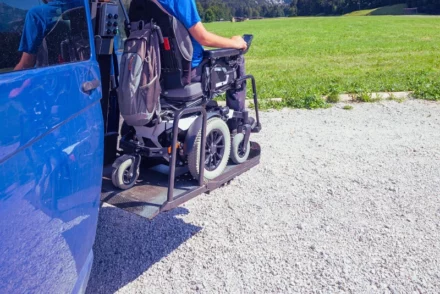 Guy wearing blue shirt on a wheelchair using wheelchair lift from a car.