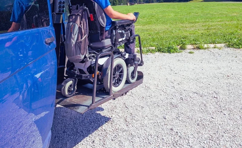 Guy wearing blue shirt on a wheelchair using wheelchair lift from a car.
